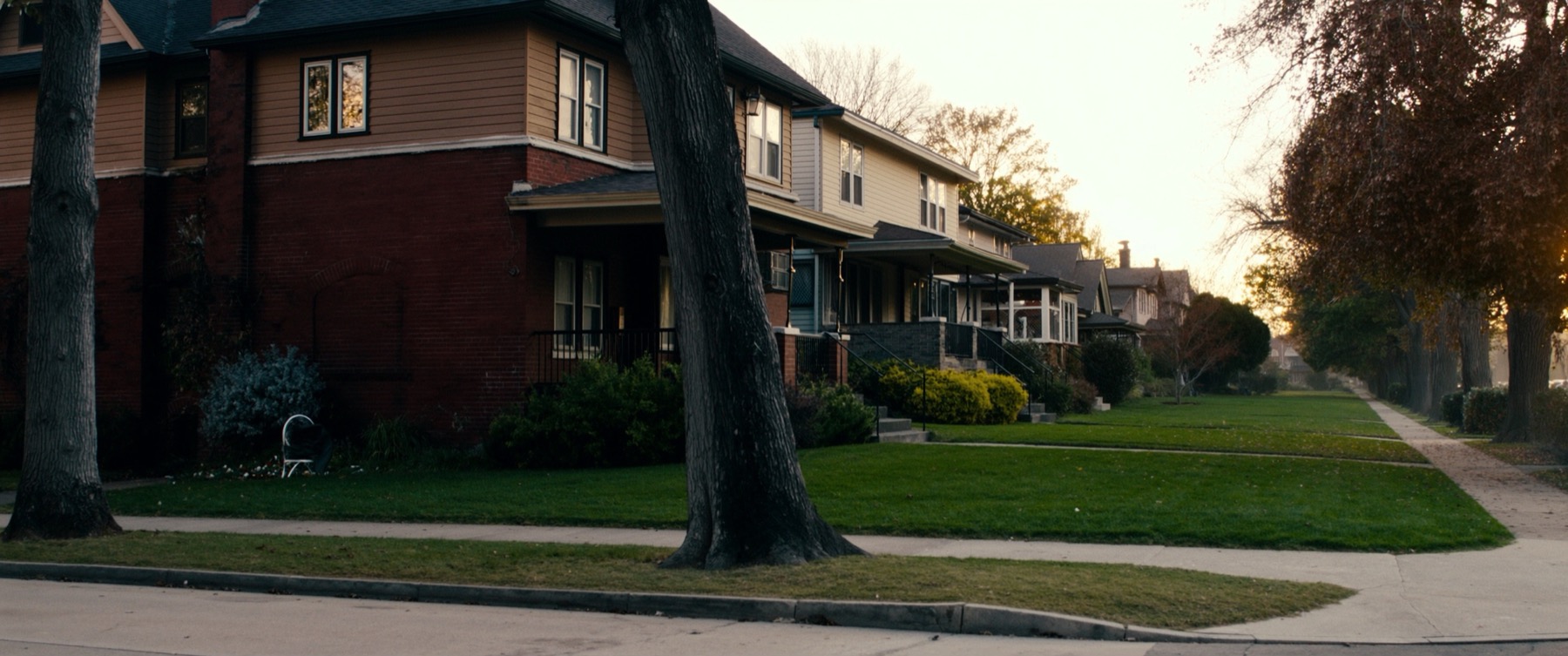 Tree-lined residential street of classic two-story American homes at golden hour